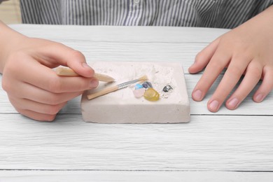 Photo of Child playing with Excavation kit at white wooden table, closeup. Educational toy for motor skills