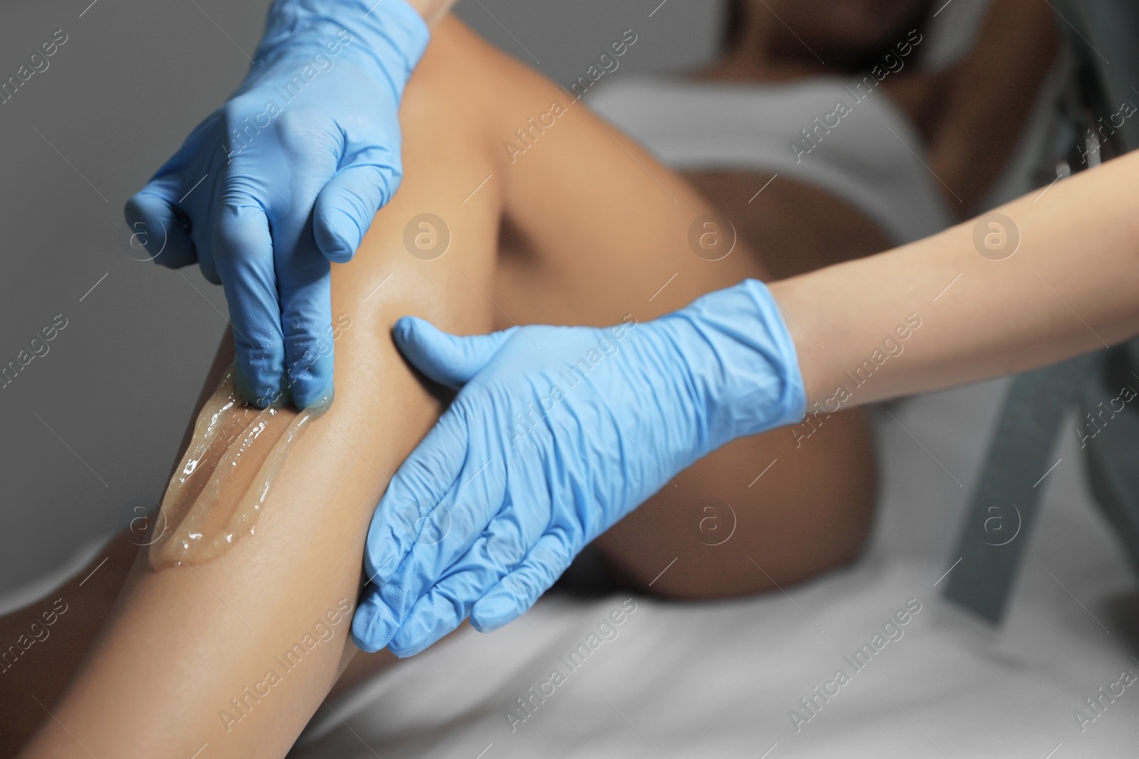 Photo of Young woman undergoing hair removal procedure on legs with sugaring paste in salon, closeup