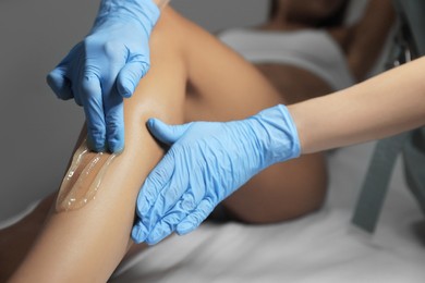 Photo of Young woman undergoing hair removal procedure on legs with sugaring paste in salon, closeup