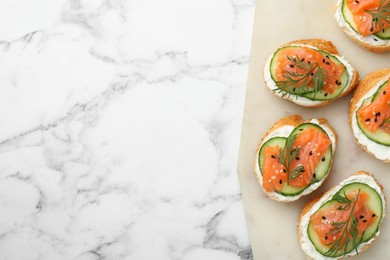 Photo of Tasty canapes with salmon, cucumber and cream cheese on white marble table, top view. Space for text