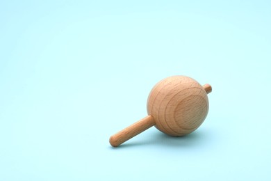 Photo of One wooden spinning top on light blue background, space for text. Toy whirligig