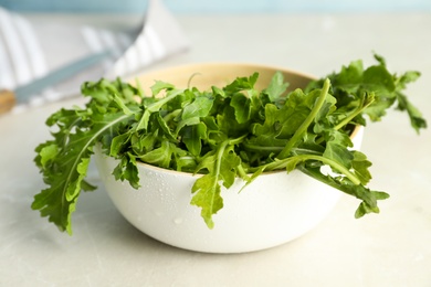 Fresh arugula in bowl on light grey table