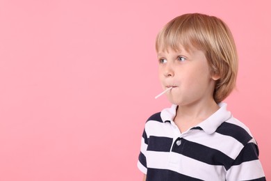 Cute little boy eating lollipop on pink background, space for text