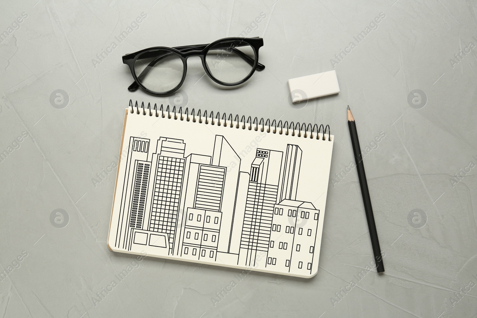 Image of Sketch of buildings in notebook, pencil, eraser and glasses on grey table, flat lay