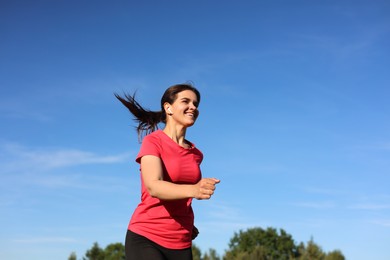 Photo of Young woman listening to music while running outdoors in morning, low angle view. Space for text