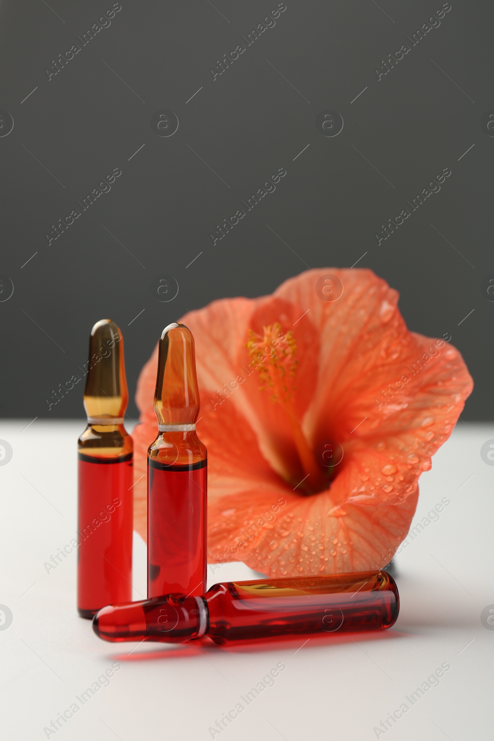 Photo of Skincare ampoules and hibiscus flower on white table