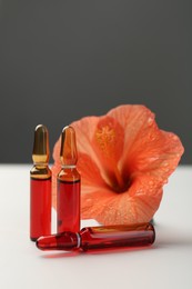 Skincare ampoules and hibiscus flower on white table