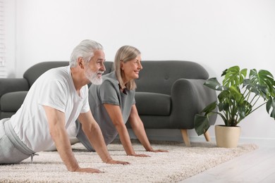 Photo of Senior couple practicing yoga on carpet at home. Space for text