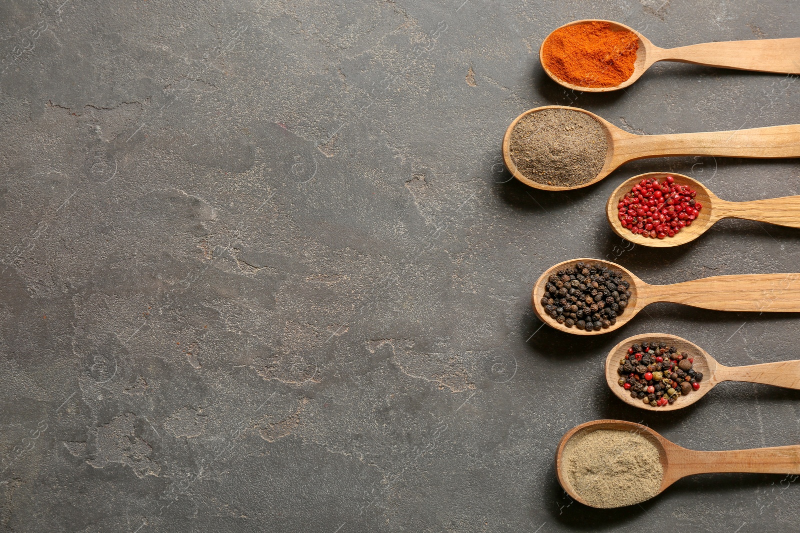 Photo of Spoons with different types of pepper and space for text on gray background