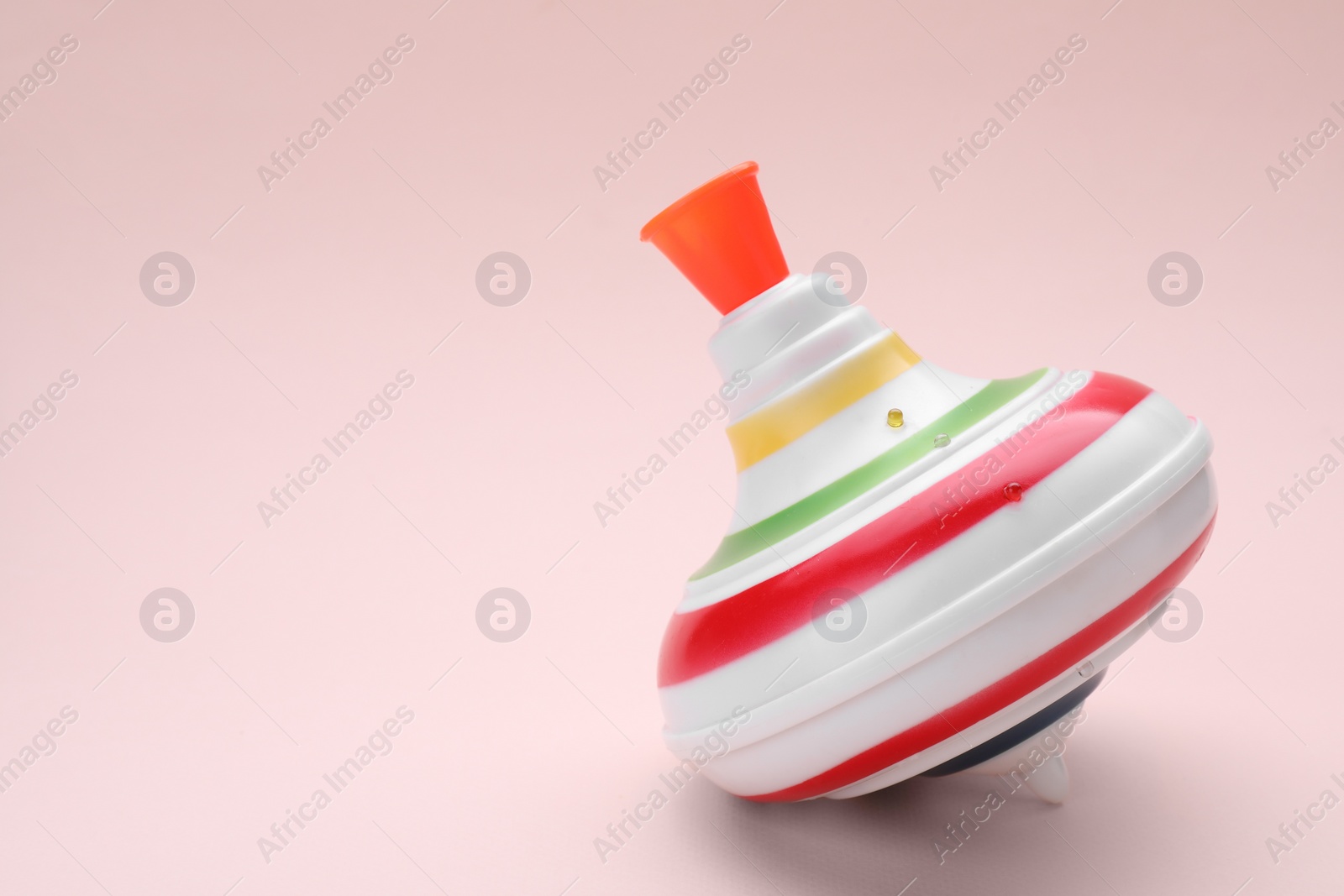 Photo of One bright spinning top on beige background, space for text. Toy whirligig