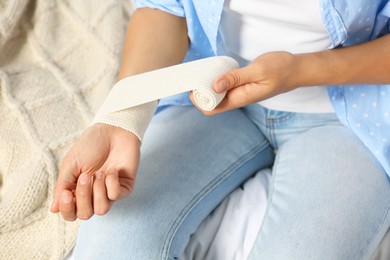 Young woman applying medical bandage onto wrist on bed, closeup