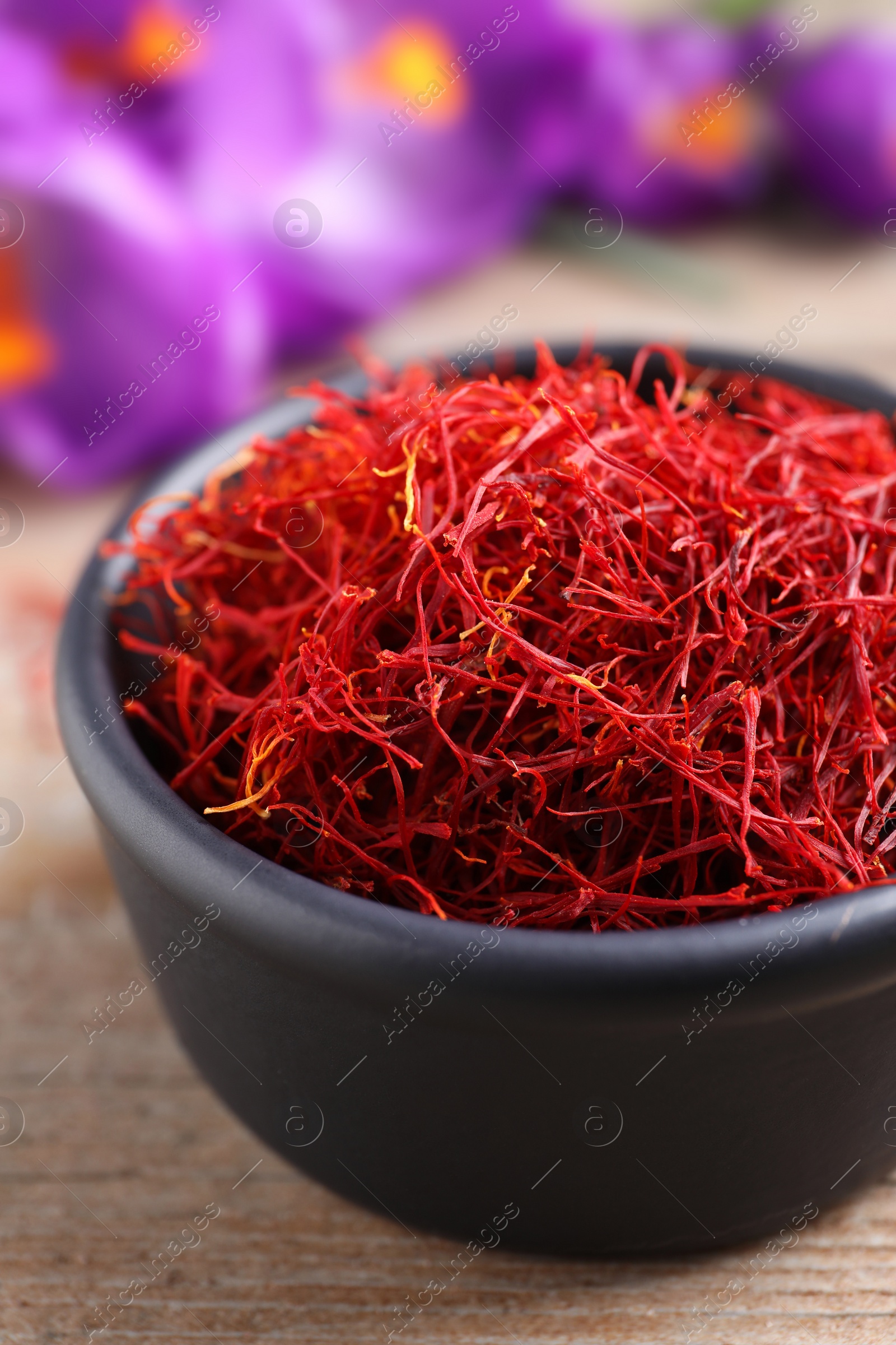 Photo of Dried saffron in bowl and crocus flowers on wooden table, closeup