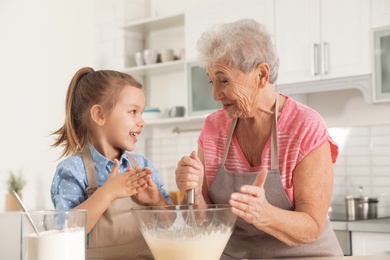 Cute girl and her grandmother cooking in kitchen