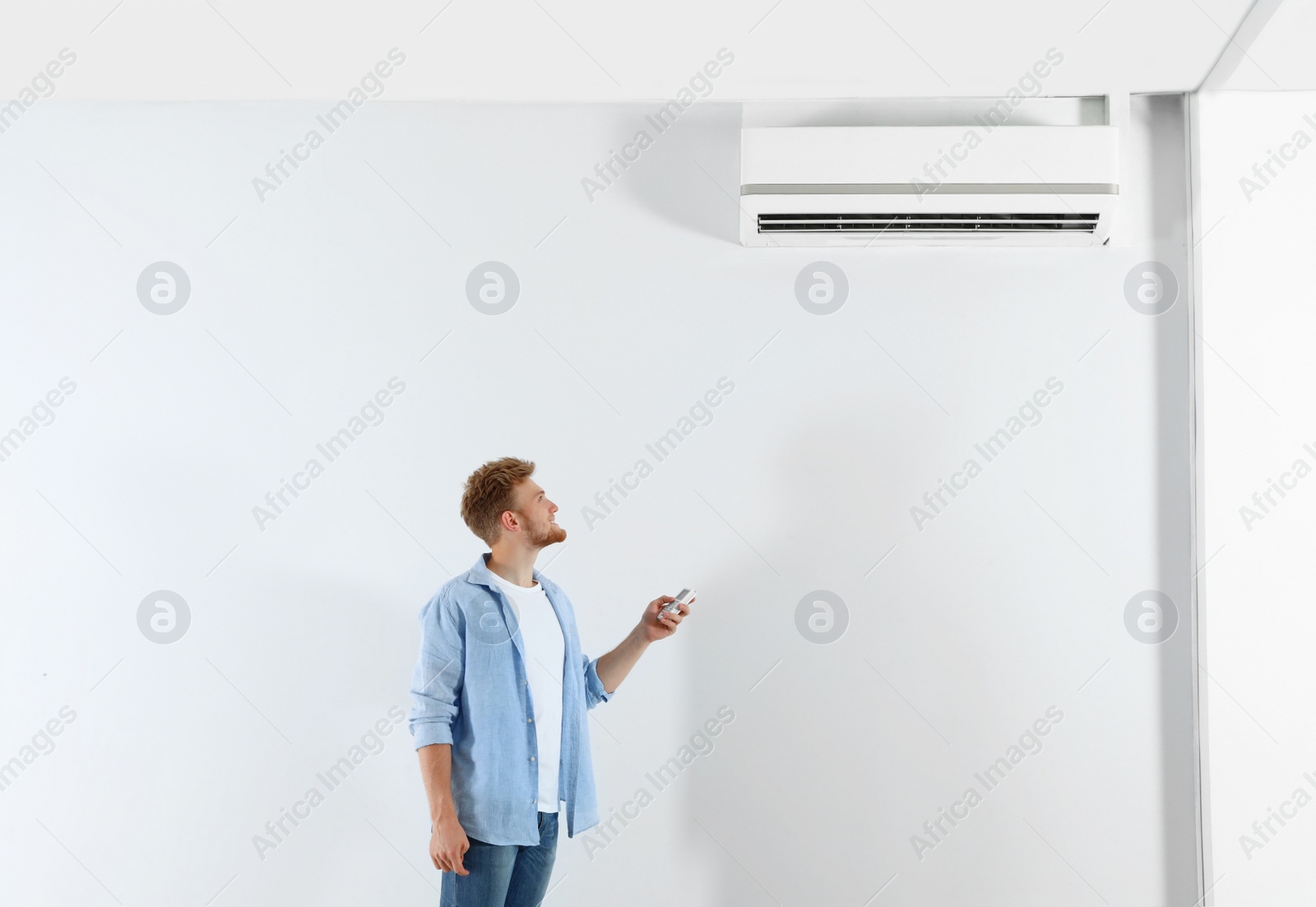 Photo of Young man operating air conditioner with remote control indoors. Space for text