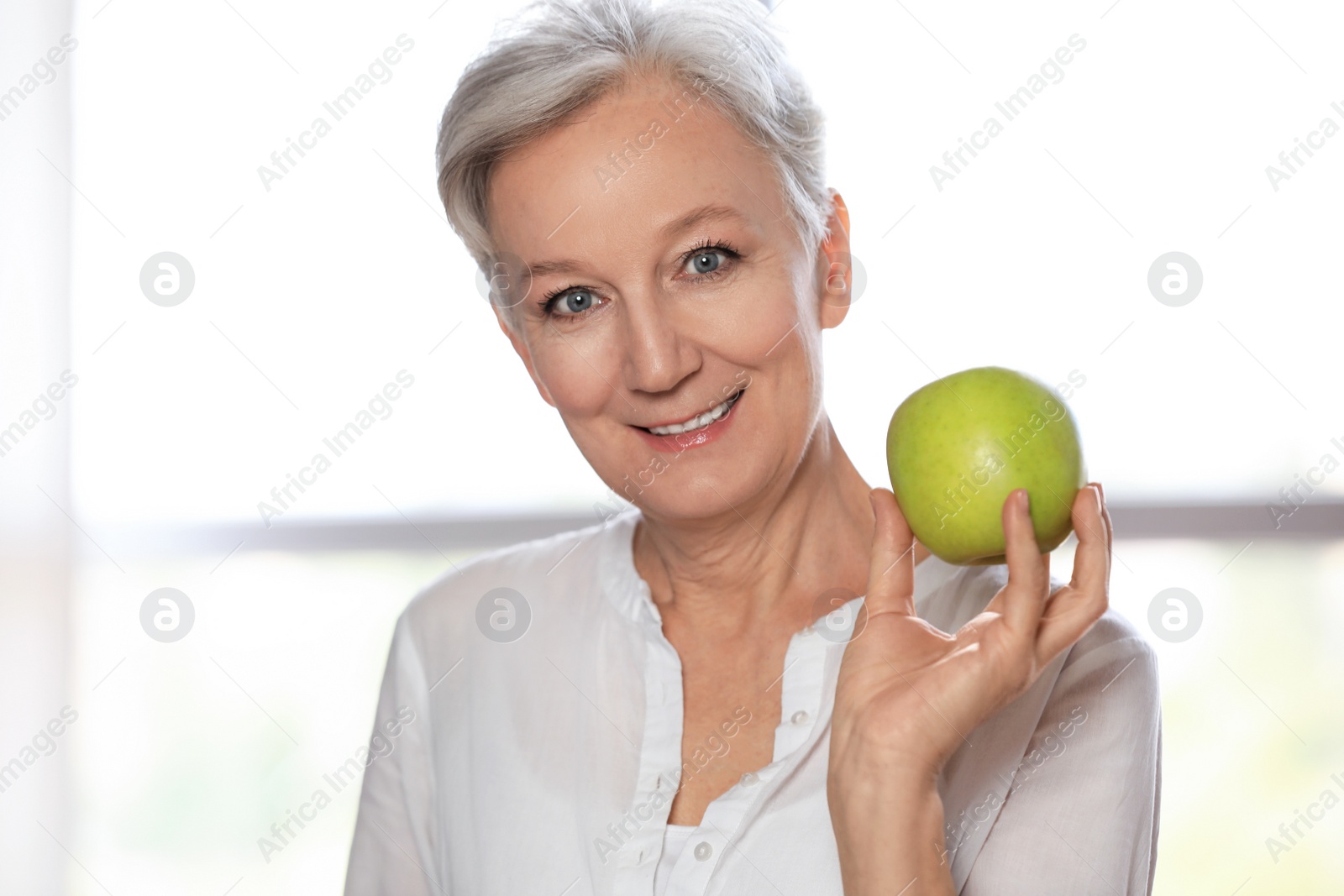Photo of Happy mature woman with green apple indoors. Smart aging