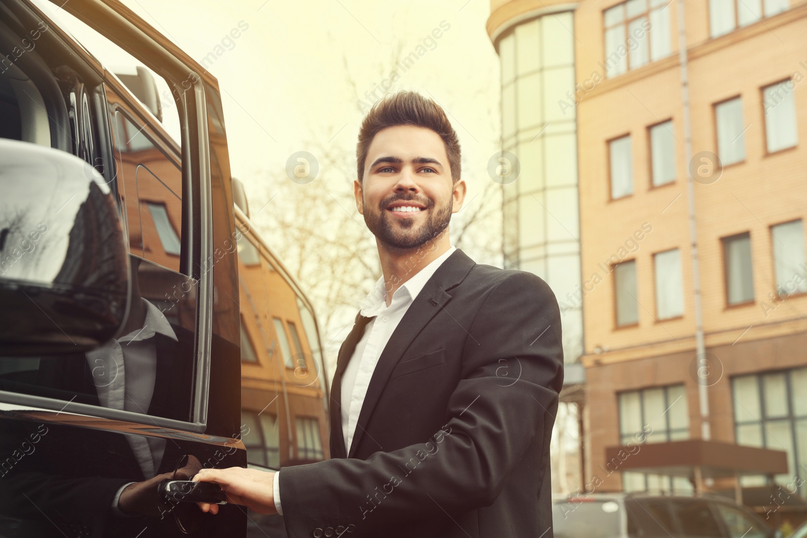 Image of Handsome young man opening door of modern car outdoors