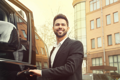 Image of Handsome young man opening door of modern car outdoors