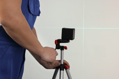 Photo of Worker pointing cross line laser level on light wall, closeup