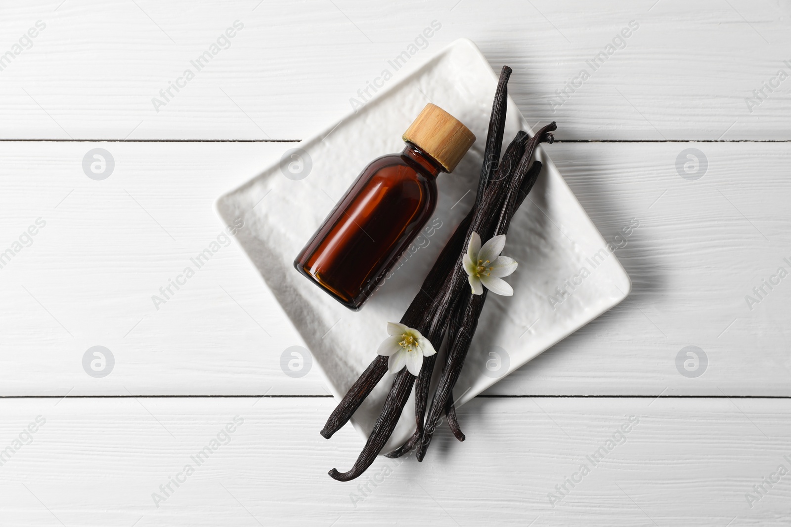 Photo of Vanilla pods, essential oil and flowers on white wooden table, top view