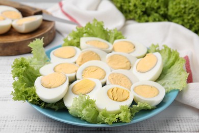 Fresh hard boiled eggs and lettuce on white wooden table