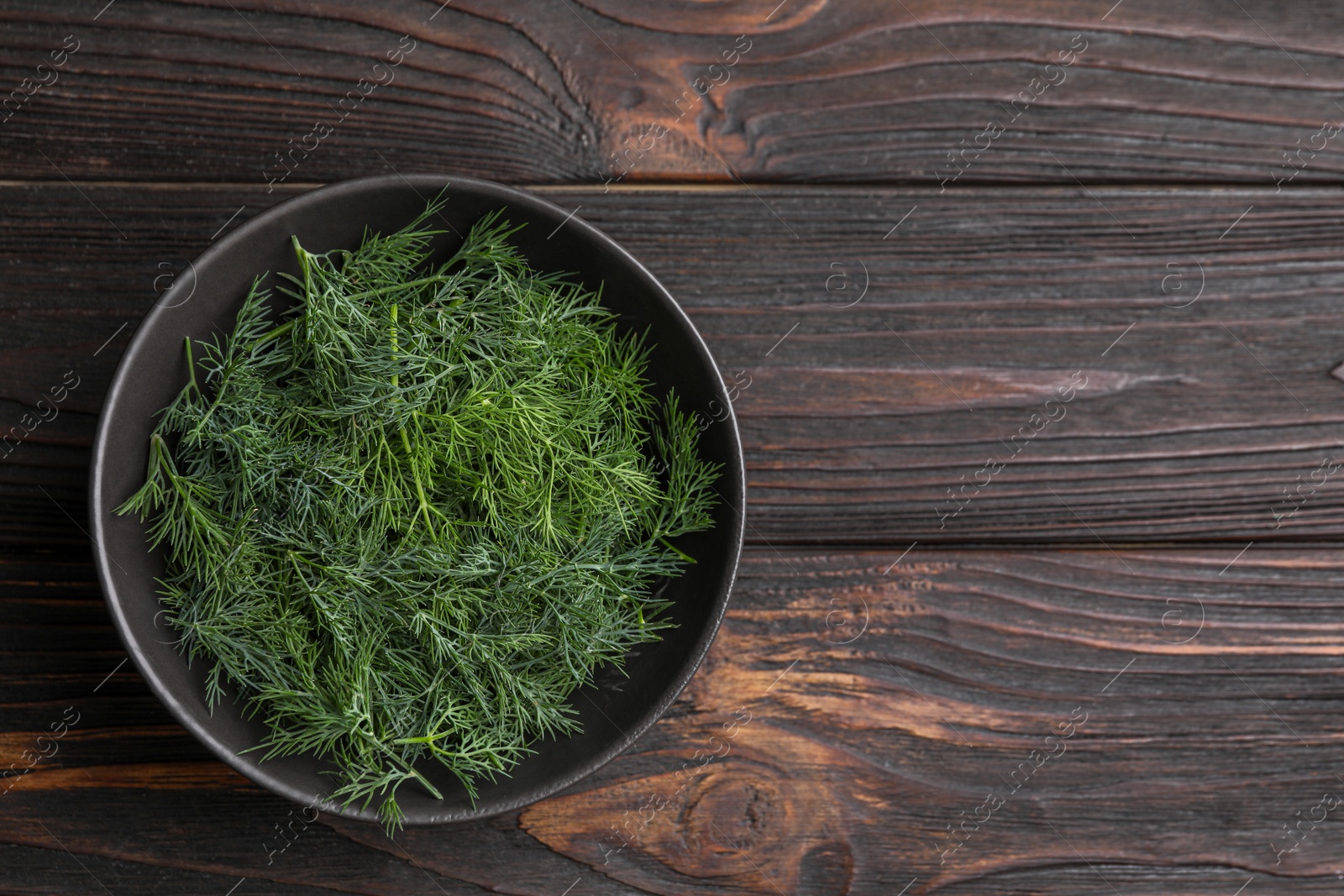Photo of Bowl of fresh dill on wooden table, top view. Space for text