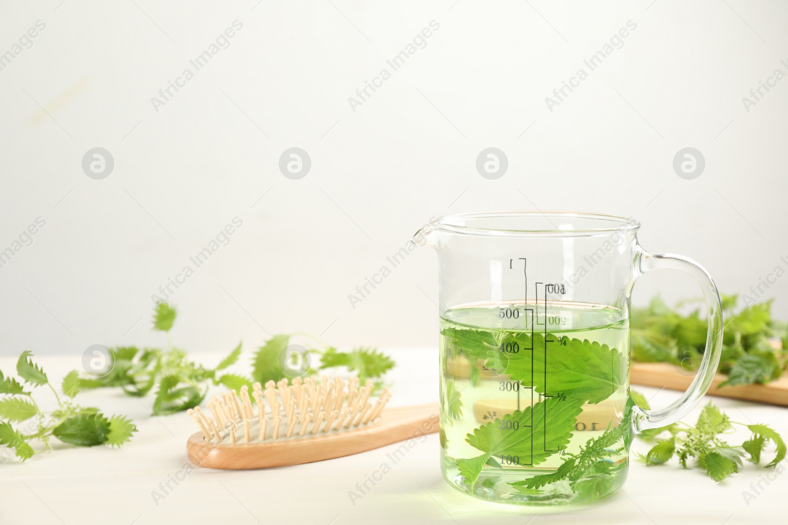 Photo of Stinging nettle extract and brush on white wooden background. Natural hair care