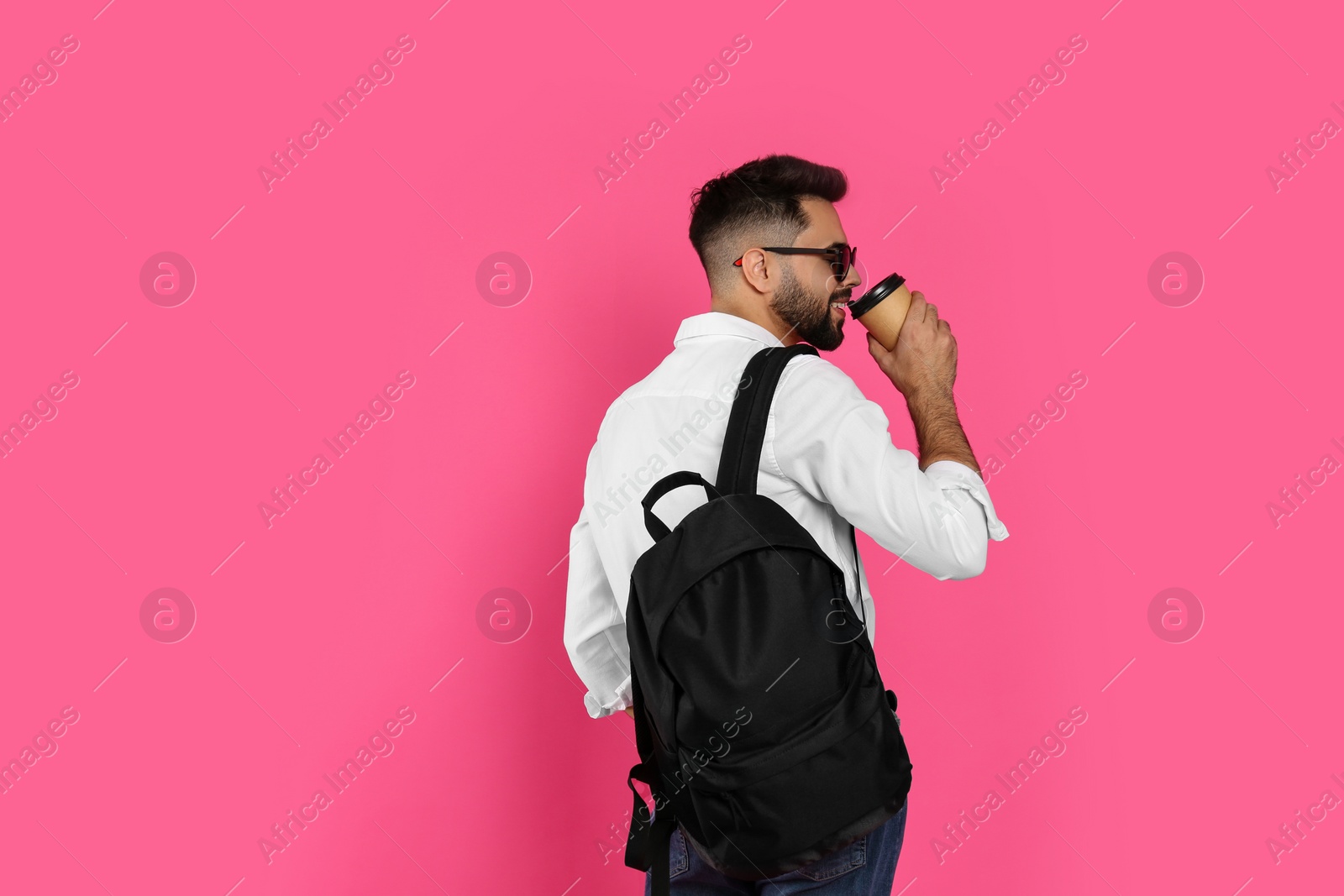 Photo of Young man with stylish backpack and cup of coffee on pink background. Space for text