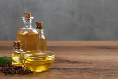 Photo of Essential oil and dried cloves on wooden table. Space for text