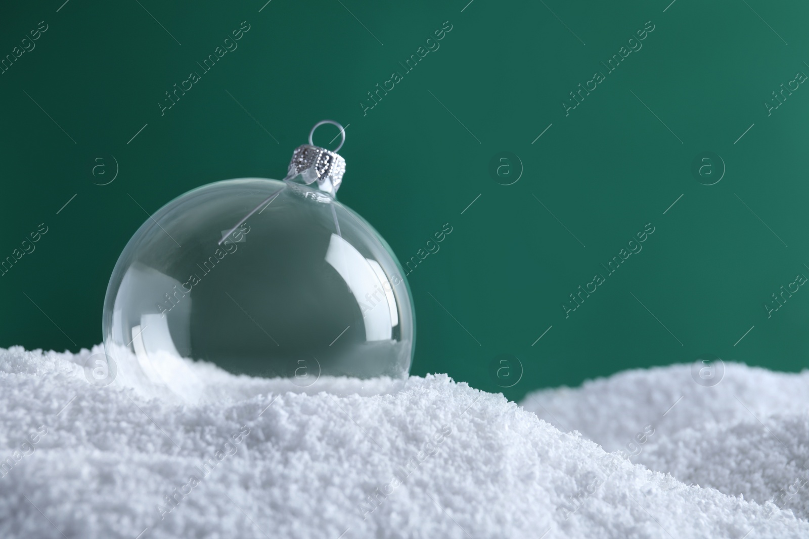 Photo of Transparent Christmas ball on snow against green background, space for text