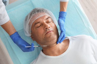 Photo of Mature man with double chin receiving injection in clinic, above view