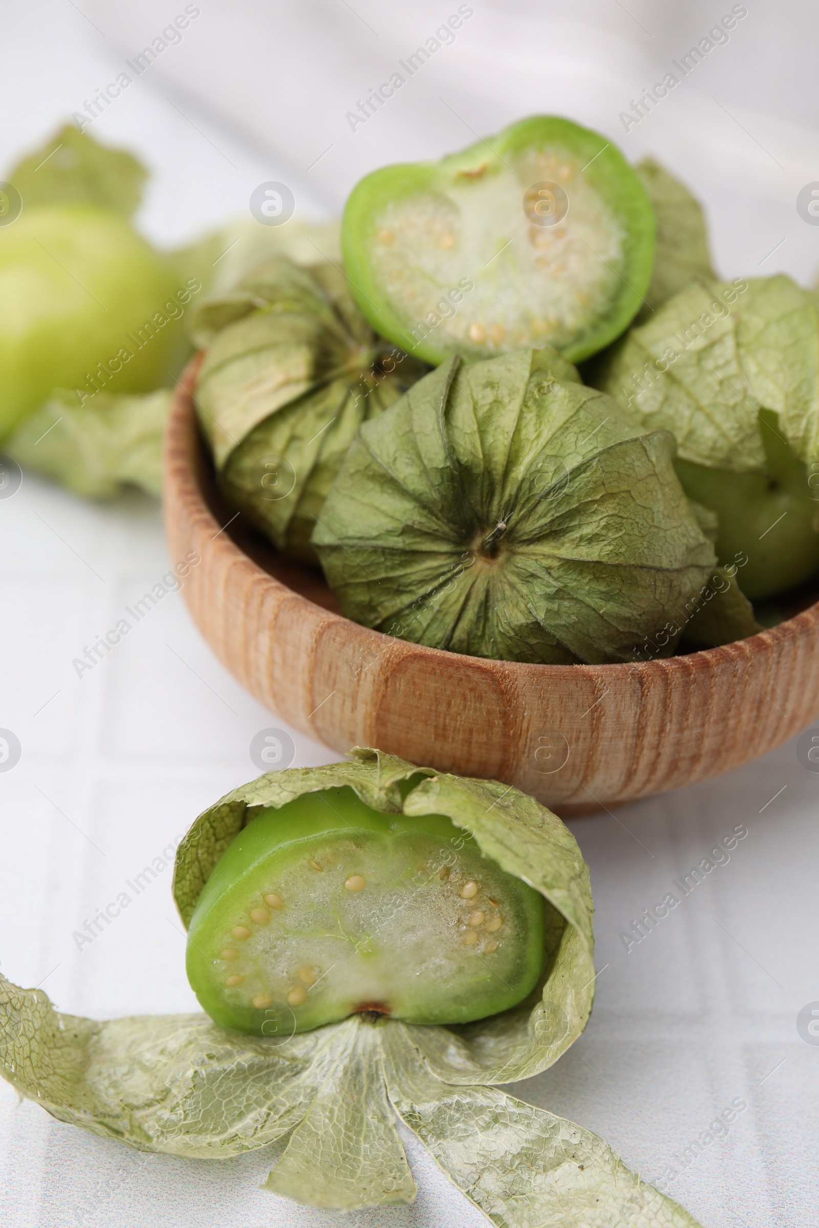 Photo of Fresh green tomatillos with husk in bowl on light table, closeup