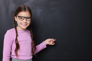 Photo of Cute schoolgirl in glasses near chalkboard, space for text