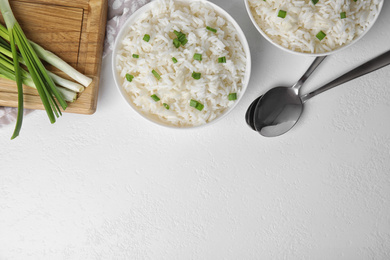 Photo of Bowls with tasty cooked rice on white table, flat lay. Space for text