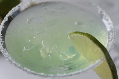 Delicious Margarita cocktail with ice cubes in glass and lime, closeup