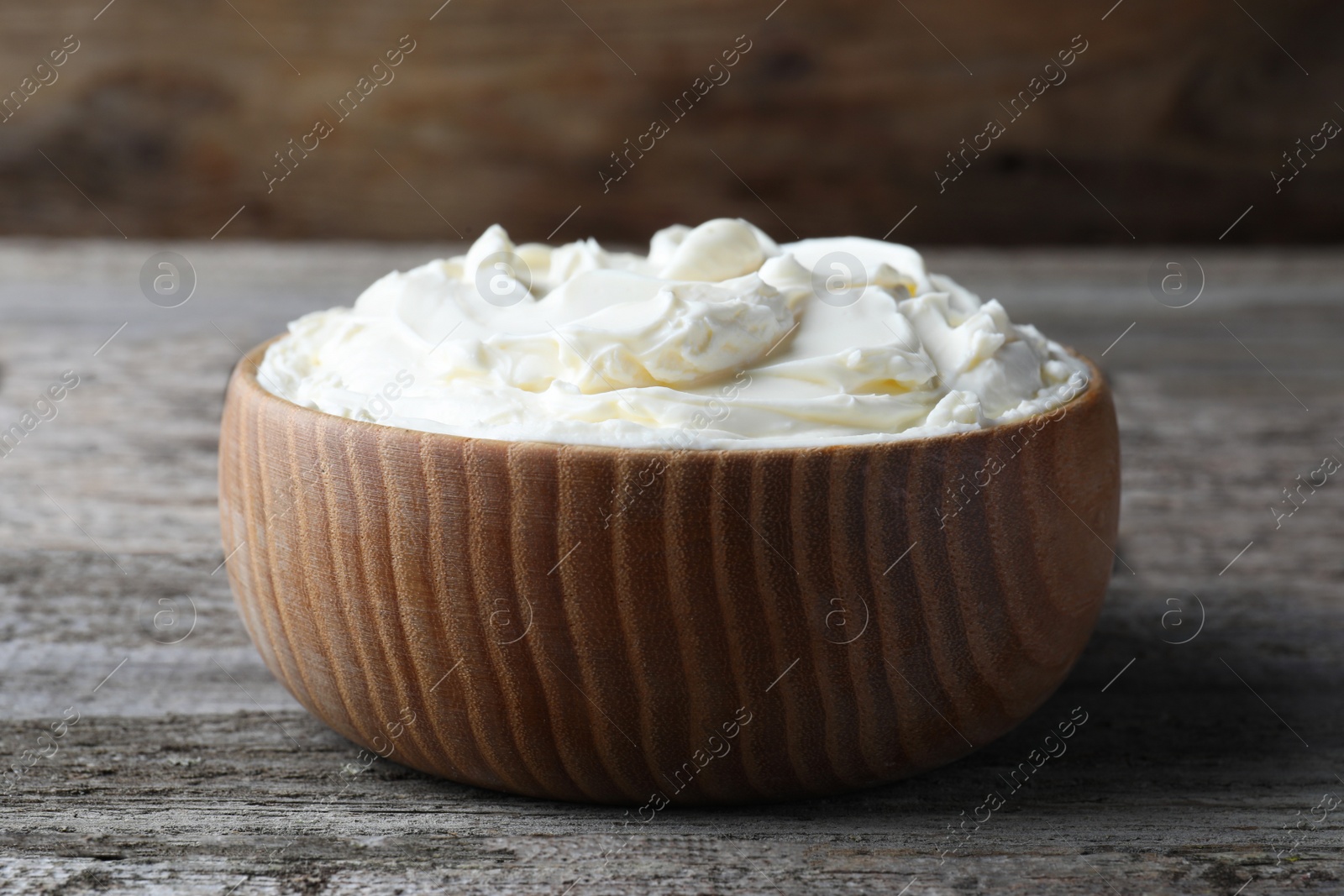 Photo of Bowl of tasty cream cheese on wooden table, closeup