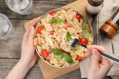 Photo of Woman eating delicious pasta with tomatoes, basil and parmesan cheese at wooden table, top view