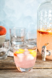 Photo of Peach cocktail in glass and jar with tap on table. Refreshing drink