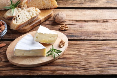 Photo of Tasty cut brie cheese with rosemary, bread and nuts on wooden table, space for text