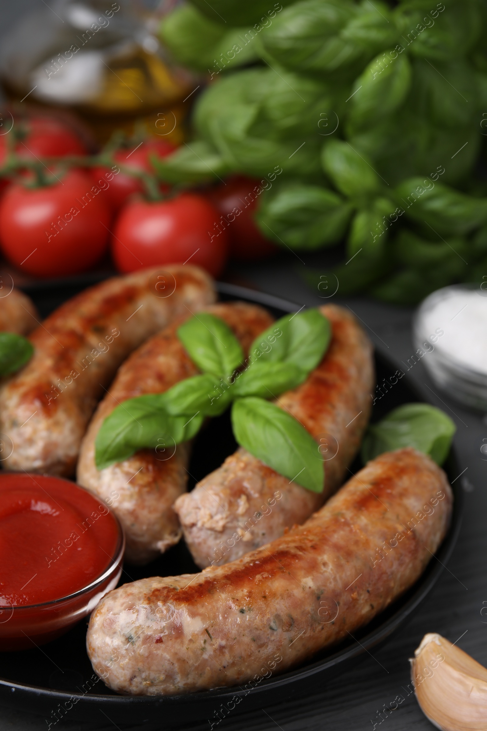 Photo of Tasty homemade sausages, ketchup and basil leaves on grey wooden table, closeup