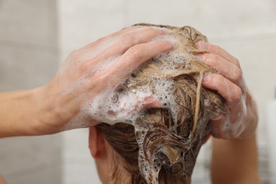 Woman washing hair with shampoo indoors, closeup