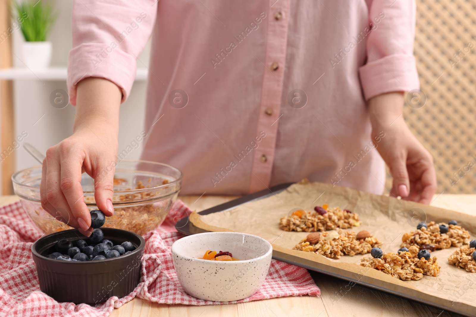 Photo of Making granola bars. Woman with blueberries at table in kitchen, closeup