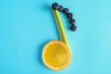 Photo of Musical note made of celery, lemon and berries on color background, top view