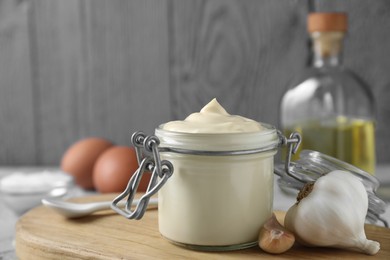 Photo of Tasty mayonnaise in jar and garlic on table, closeup. Space for text