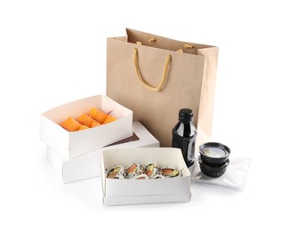 Photo of Food delivery. Boxes with delicious sushi rolls, paper package and soy sauce on white background