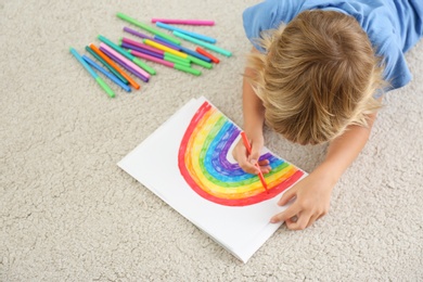 Photo of Little boy drawing rainbow on floor indoors, above view. Stay at home concept