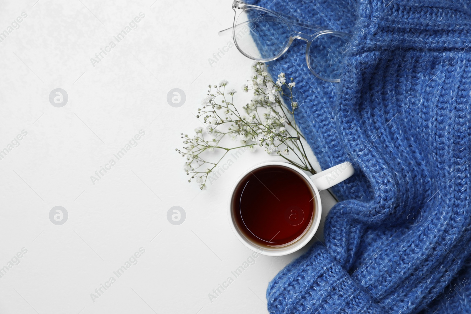 Ceramic mug with aromatic tea, blue knitted sweater, glasses and beautiful dry flowers on white background, flat lay. Space for text Photo of Ceramic mug with aromatic tea, blue knitted sweater, glasses and beautiful dry flowers on white background, flat lay. Space for text