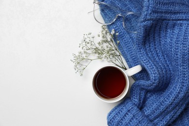 Photo of Ceramic mug with aromatic tea, blue knitted sweater, glasses and beautiful dry flowers on white background, flat lay. Space for text