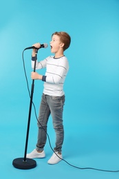 Cute boy singing in microphone on color background