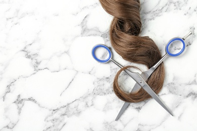 Photo of Flat lay composition with strand of brown hair, scissors and space for text on marble background. Hairdresser service