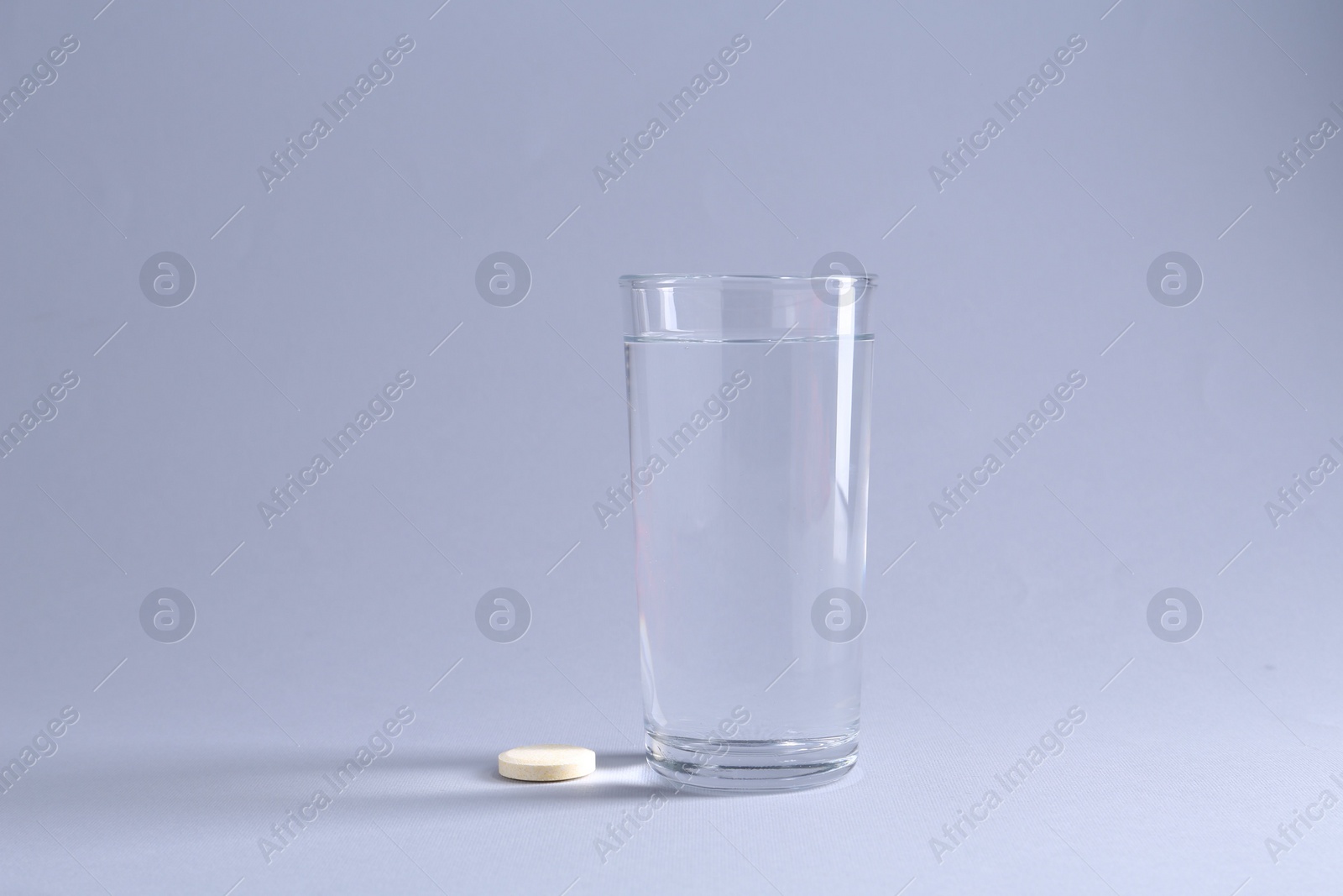 Photo of Effervescent pill and glass of water on light grey background